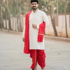 A classic portrait of a groom in traditional Marathi attire. The simple, clean background allows his vibrant red dhoti and serene expression to take center stage.