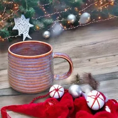 This cozy, hand-built mug features a warm, earthy glaze with hints of purple. The comfortable handle and unique form are reminders of the hands that shaped it.