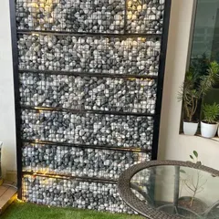 A detailed look at the illuminated gabion wall. The combination of industrial wire mesh, natural stones, and warm backlighting creates a unique feature that is both rustic and modern.