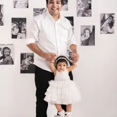 A proud father helps his daughter stand tall. The minimalist background with a personal photo gallery wall adds a unique touch without being distracting.