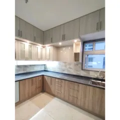 This simple and functional L-shaped kitchen is designed for modest living. The dual-tone laminate cabinets in light wood and grey offer ample storage, while under-cabinet lighting ensures a well-lit workspace.