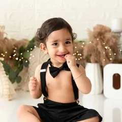 A charming portrait of a little boy dressed in a bow tie and suspenders, part of a boho-themed first birthday shoot.