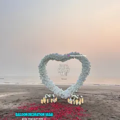 This wide shot shows the full scale of the beach proposal decoration. The heart arch stands as a beautiful centerpiece on the sand, with a path of red rose petals leading up to it, making for a grand and romantic gesture.
