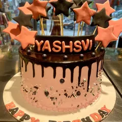 A stylish pink and black drip cake perfect for a chic birthday celebration. This cake is topped with a burst of pink and black stars and features a rich chocolate drip over light pink frosting.