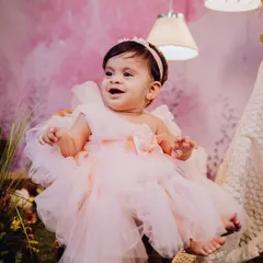 A sweet portrait of a baby girl dressed as a little princess in a fluffy pink dress. The soft, pastel-colored backdrop creates a gentle and charming setting.