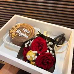 This birthday hamper features a delicious chocolate bento cake topped with hazelnuts, paired with a mini bouquet of red roses and Ferrero Rocher. It's a classic combination for a special celebration.