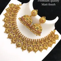 A beautiful temple necklace set with matching jhumkas. The design features tiny goddess figures and peacock motifs with red and green stones, all in a premium matte finish.