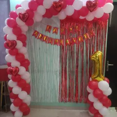 A classic full balloon arch for a first anniversary. I used red and white balloons, heart-shaped foils, a fringe curtain, and a number "1" balloon column to create a complete photo backdrop.