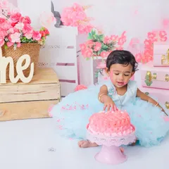 A moment of discovery during a first birthday cake smash. This little girl in a blue tutu curiously touches her pink cake, a sweet and candid shot from her special day.