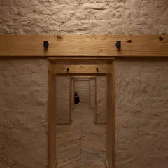 Inside the Rung Community Museum, a perspective of repeating doorways framed by local pine wood and textured mud-plastered walls creates a journey through the restored space, honoring its past.