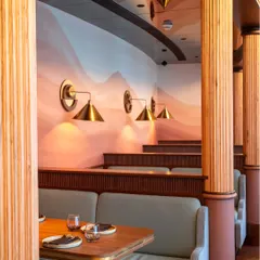 The warm and inviting seating arrangement at Comorin. This shot highlights the beautiful textures of the wood, the soft lighting, and the artistic wall mural, creating a sense of comfort and style.