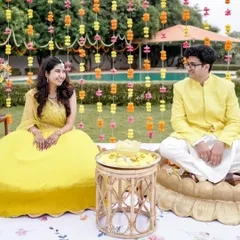 A candid moment during a Haldi ceremony, set against a backdrop of hanging marigold and carnation garlands.