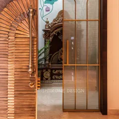 The entrance to the sacred space is just as important as the space itself. Here, a beautifully crafted wooden door with a fan-like pattern and a sleek glass door with brass trim lead into the mandir.