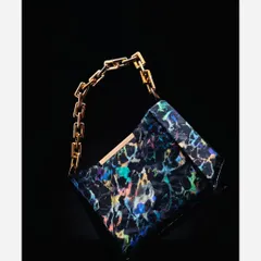 This luxury handbag is shot against a pure black background to emphasize its unique, iridescent pattern and gold chain. The lighting is carefully controlled to highlight the product's form and texture without reflections.