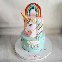 A magnificent two-tier unicorn cake for a 5th birthday. The bottom tier is a lovely pastel blue, while the top tier features a beautiful unicorn head with a colorful mane.