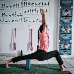 A student practices Virabhadrasana I, or Warrior I pose, using a block for stability. This demonstrates our focus on proper alignment and the use of props to build a strong foundation, which is essential for future teachers.