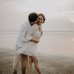 A candid and joyful pre-wedding moment on the beach, with the groom kissing the bride's cheek as she laughs.