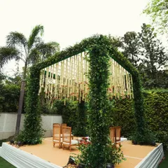 This mandap is designed to blend with nature, featuring pillars completely covered in lush greenery. The roof is decorated with hanging strings of white flowers, creating a beautiful rustic-chic look.