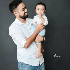 A classic studio portrait of a father holding his young son. The simple dark grey background and professional lighting put the focus entirely on their happy interaction.