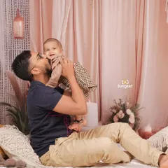 A heartwarming moment between a father and his baby during a sitter session. The gentle kiss and the baby's happy smile are perfectly captured in our cozy, boho-themed studio setup.