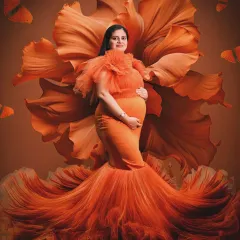 A vision in orange. This portrait features a stunning orange gown that blends into a large, artistic flower backdrop, creating a vibrant and cohesive artistic statement.
