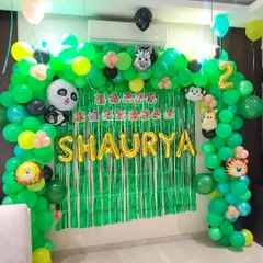 A lush jungle-themed birthday decoration for a two-year-old. I created a full balloon arch in shades of green to mimic a jungle canopy, accented with cute animal foil balloons like a panda, zebra, and lion. The green shimmer backdrop and gold foil name "SHAURYA" make this a fun and adventurous photo corner.