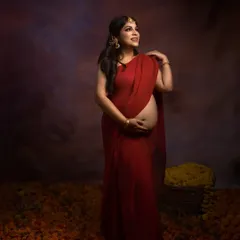 A portrait of grace. This standing pose in a red saree, surrounded by marigolds, is a timeless tribute to Indian traditions and the strength of motherhood.