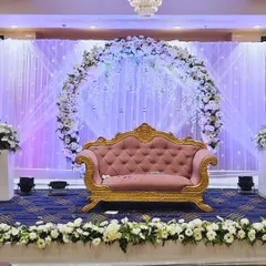 An elegant stage for a ring ceremony or engagement party. The design features a large circular arch of white flowers, delicate hanging crystals, and a backdrop of white drapes with fairy lights.