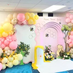 The full backdrop for the Winnie the Pooh Aqeeqa, featuring a large balloon arch in pastel pink and yellow, and a custom-designed Hundred Acre Wood scene.