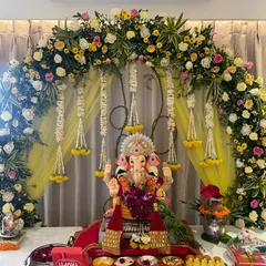 A traditional Ganpati decor setup with a vibrant arch of yellow and pink flowers, complemented by hanging jasmine strings.