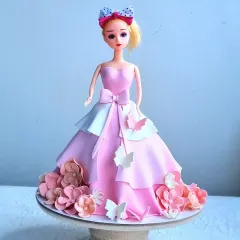A classic Barbie doll cake, where the cake itself forms the doll's beautiful, flowing gown. The dress is decorated with pink and white fondant layers, a bow, and flowers.