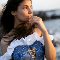 A close-up portrait that feels candid and thoughtful. The wind in the hair and the soft, natural light create an intimate mood, perfect for showcasing the details of the ruffled, off-the-shoulder top.