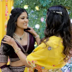A sweet moment between sisters. The bride's makeup is soft and radiant, designed to complement her deep purple lehenga without overpowering her features.