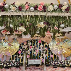 A detailed shot of the whimsical butterfly naming ceremony stage. The hanging paper flowers, clouds, and disco balls add layers of texture and fun to the overall design.
