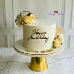 Elegant and timeless, just like their love. A beautiful white and gold anniversary cake for 'Mom & Dad', featuring a delicate texture and floral accents.
