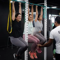 Training is better with friends. Three of our members work on their pull-up strength, using the bar for dead hangs while a coach guides them. This shows how we use partner and group work to make training social and effective.