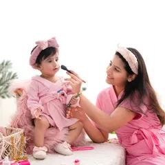 A playful spa day for mother and daughter. Dressed in matching pink robes, they share a fun moment with makeup brushes, creating a unique and adorable memory.