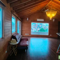 The interior of a rustic wooden cottage built on a terrace in New Friends Colony. The room is paneled with natural wood, creating a warm and cozy cabin-like feel.