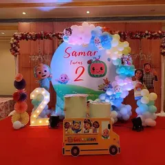 A fun Cocomelon theme for a second birthday party. The setup includes a round backdrop, a light-up number '2', and a prop of the iconic yellow school bus from the show.