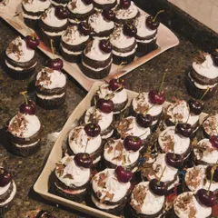 A whole spread of my Black Forest cupcakes, ready for a party. Each one is a mini cake with layers of chocolate sponge, cream, and cherry filling, topped with a fresh cherry.