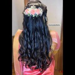 A half-up, half-down hairstyle with beautiful, bouncy curls. The look is finished with a barrette of fresh pink roses and baby's breath for a touch of elegance.