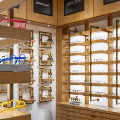 The display units feature a mix of wood and metal, with integrated lighting to showcase the luxury eyewear brands. The design creates a sophisticated and inviting atmosphere for customers.