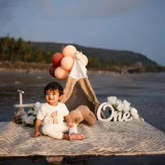 A happy one-year-old enjoying his boho-themed beach setup. The combination of the teepee, balloons, and the sea makes for a stunning backdrop.
