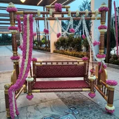 An ornate wooden swing (jhoola) decorated with pink and white floral garlands, serving as a beautiful and traditional seating option for the bride during her Mehendi ceremony.