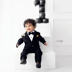 A full-body shot of this dapper one-year-old, capturing his joyful expression as he sits on the steps next to a "1" made of balloons.
