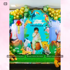 The centerpiece of this jungle party is the custom backdrop featuring the birthday boy's photo, surrounded by illustrated animals. Life-like animal props like a lion, leopard, and deer are placed in the foreground to create a layered, three-dimensional scene.