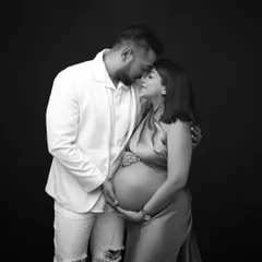 A classic black and white maternity portrait that exudes intimacy and love. The high contrast and simple background keep the focus entirely on the couple's tender embrace.