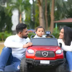 A beautiful family portrait centered around their child in his bright red toy car. A perfect snapshot of a happy family day out.
