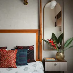 Every detail in this bedroom is a gentle nudge towards comfort. The classic four-poster bed is adorned with hand-embroidered cushions, and a floating nightstand with an arched mirror adds a touch of modern elegance.
