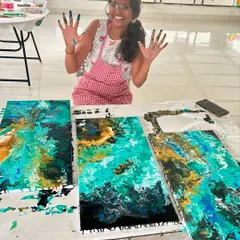 A guest joyfully shows off her paint-covered hands after an immersive fluid art session.